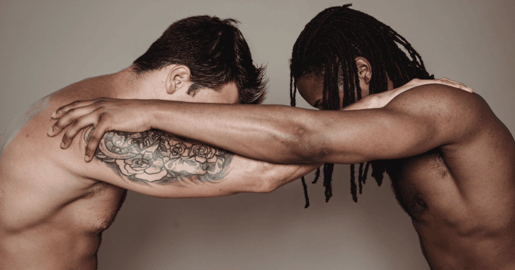 Dos hombres, uno de ellos negro, sujetándose mutuamente por los hombros y mirando hacia abajo en una postura que recuerda a una disciplina de contacto o judo.