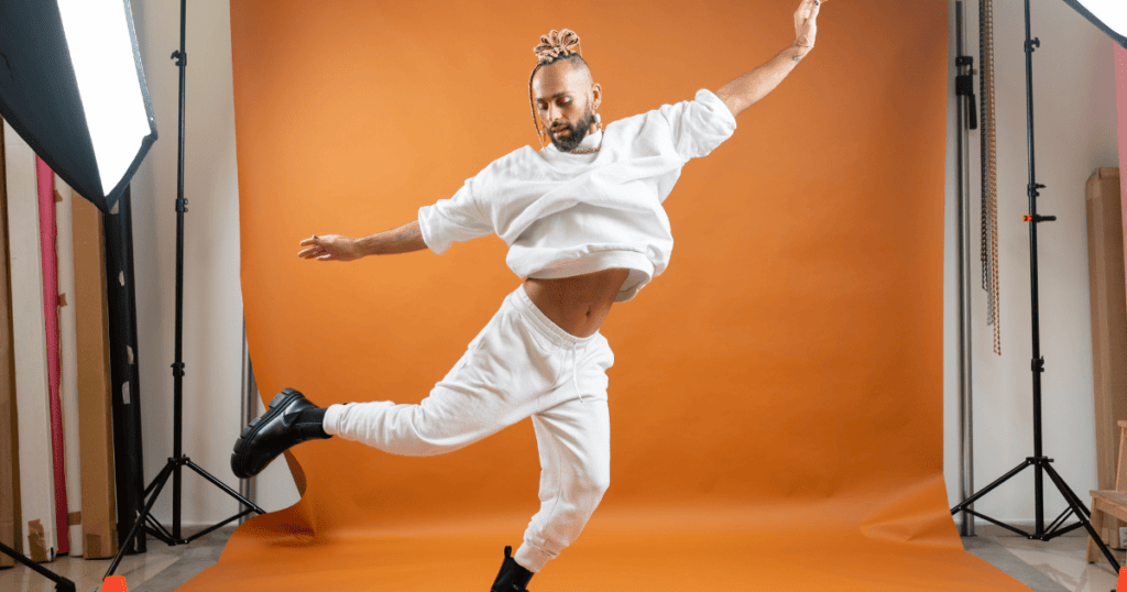 Un chico queer con ropa moderna, haciendo un pase de baile en un estudio de fotografía, simbolizando la moda como expresión de la identidad.