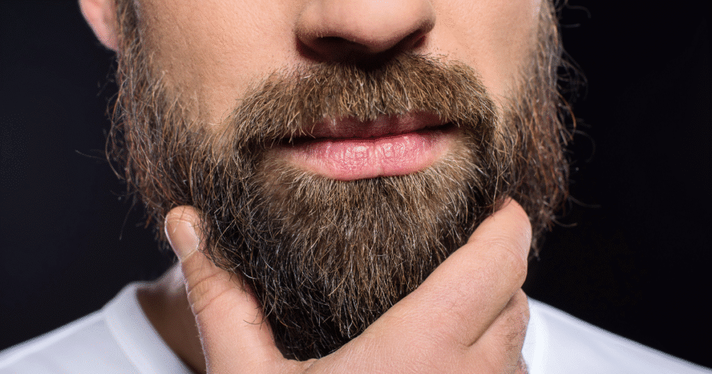 Primer plano de un hombre con una barba abundante, tocándosela pensativamente, simbolizando la pogonofilia.
