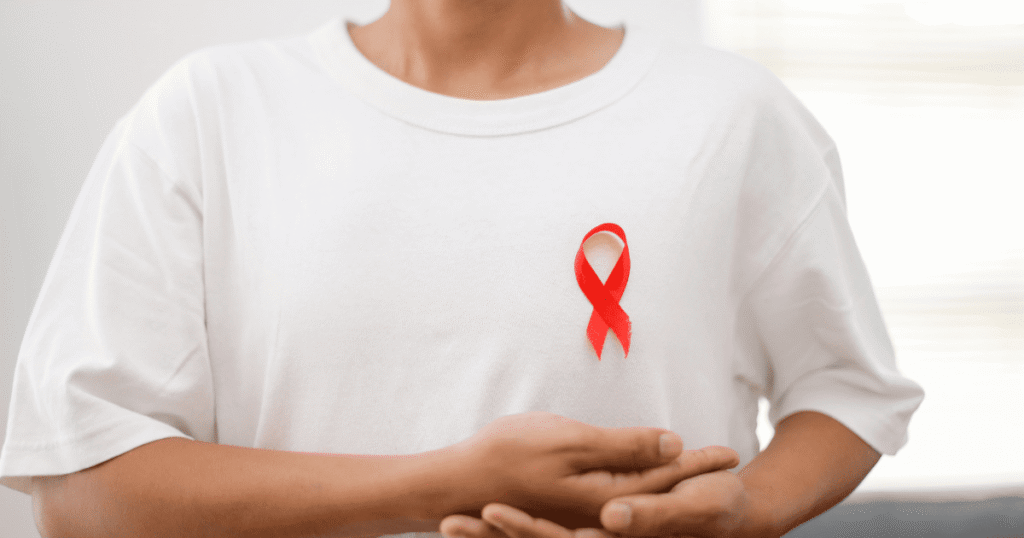 Persona con camiseta blanca y un lazo rojo, símbolo del Día Mundial de la Lucha contra el SIDA y la concienciación sobre el VIH.