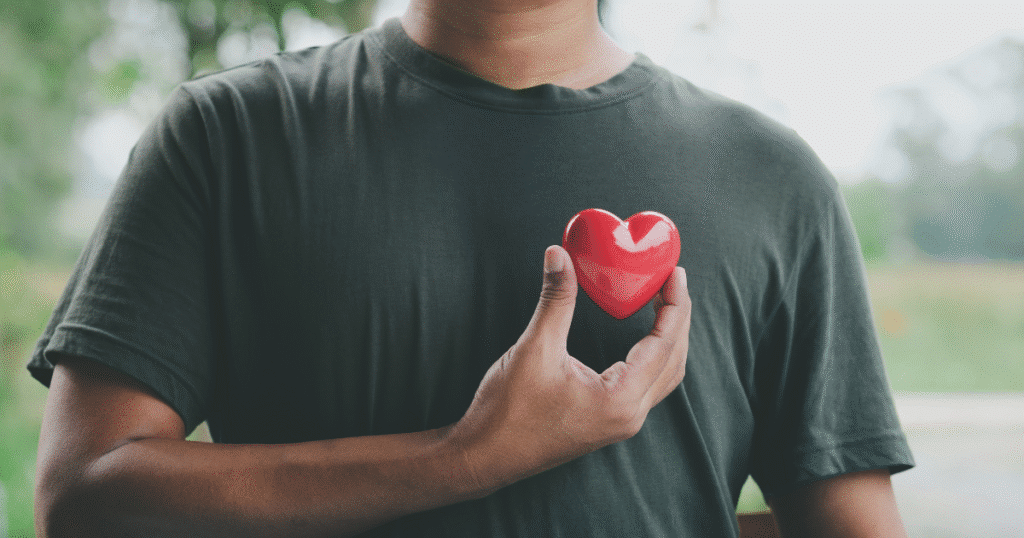 Primer plano de un hombre sosteniendo una figura con forma de corazón a la altura de su pecho, simbolizando el compromiso con la vida y la lucha contra el SIDA.